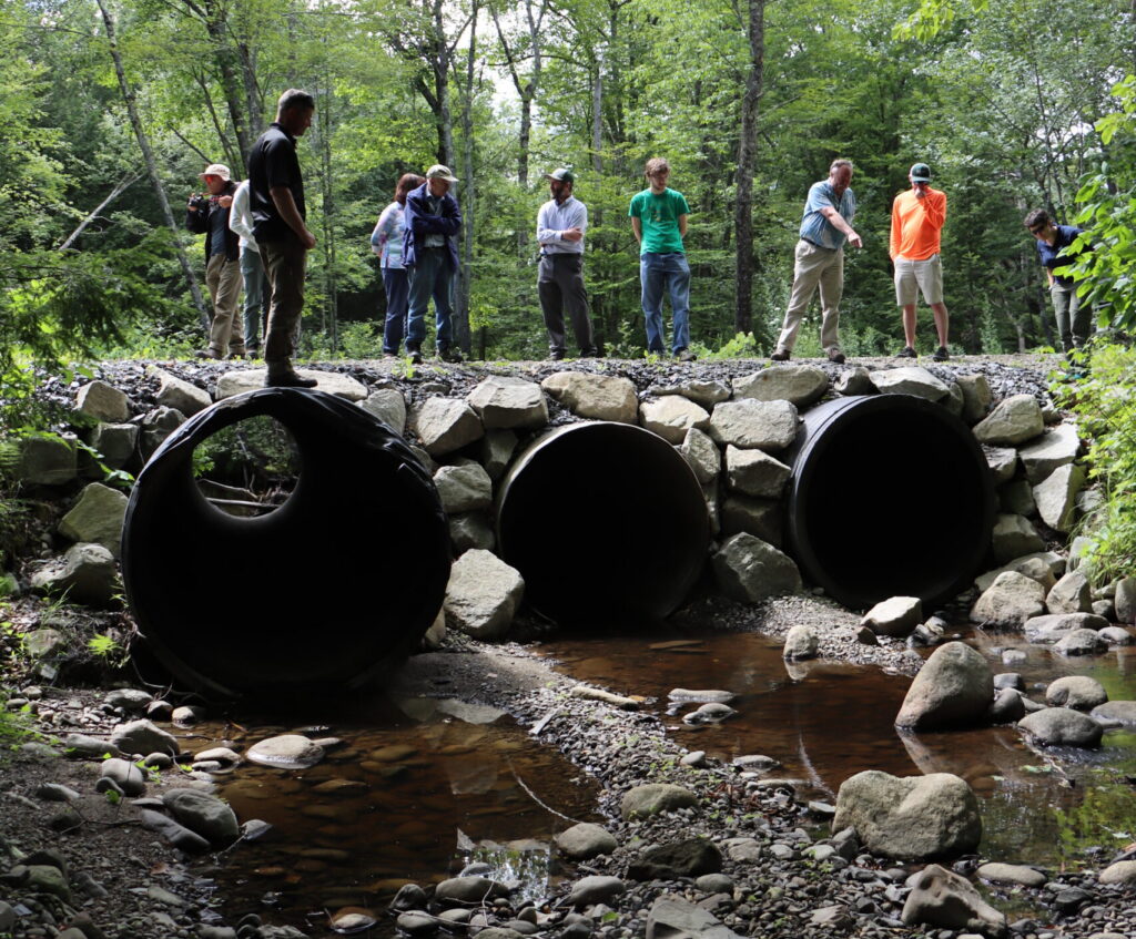 Workshop Attendees are looking at three enormous culverts. One man is standing on a culvert as tall as he is.