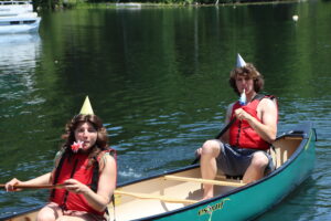 Two people in a canoe with party hats and party horns